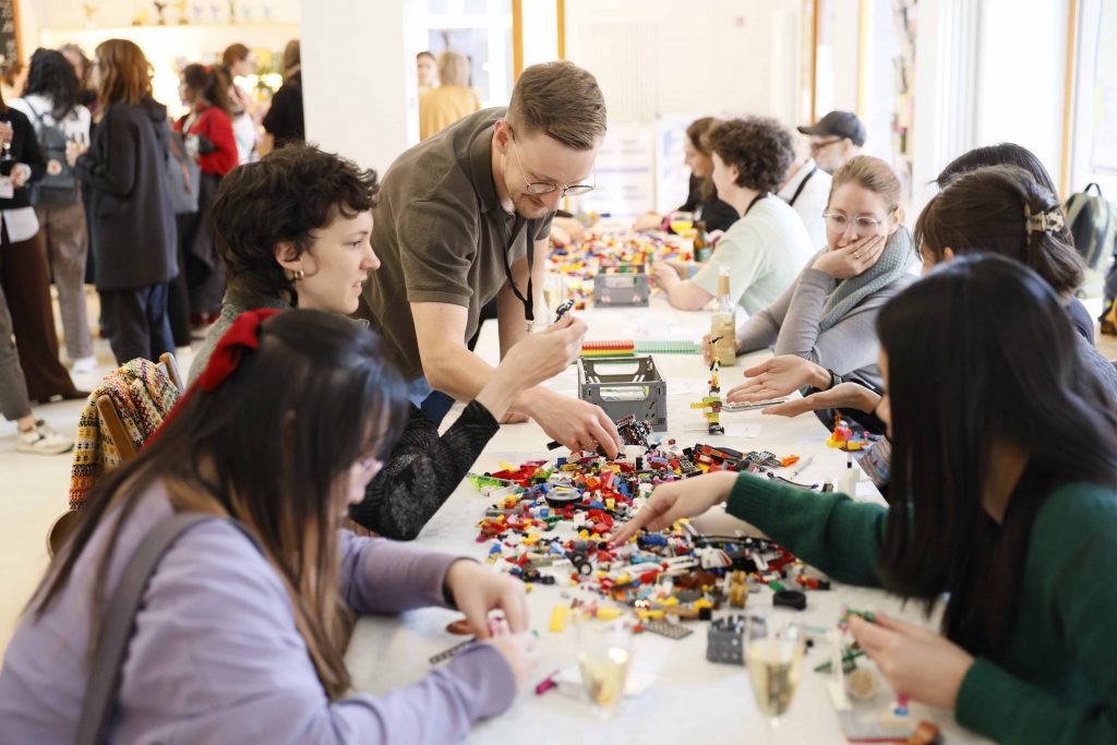 Eine Gruppe von Menschen sitzt um einen Tisch herum und bastelt mit Lego-Steinen.